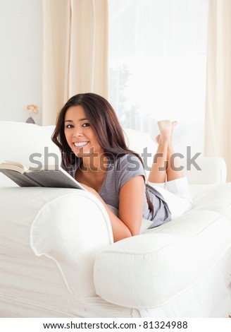 charming woman lying on sofa reading a book looking into camera in living room