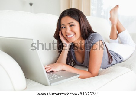 cute woman lying on sofa with notebook smiling into camera in living room