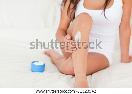 good-looking woman putting cream on her legs in bedroom