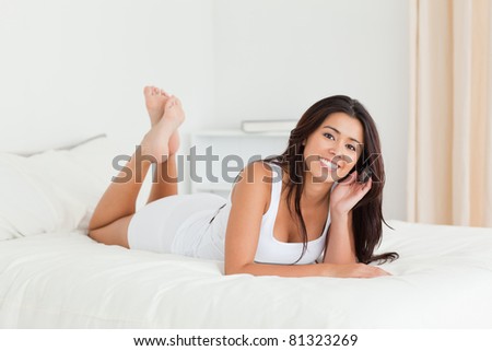 cute woman lying on bed with crossed legs looking into camera in bedroom