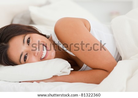 close up of a smiling cute woman lying under sheet in bedroom