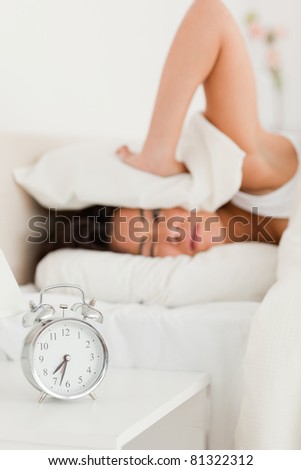 cute woman waking under sheet not wanting to hear alarm clock in bedroom