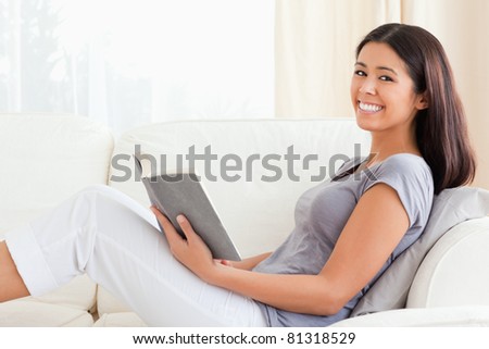 young woman reading a book sitting on sofa smiles into camera in living room