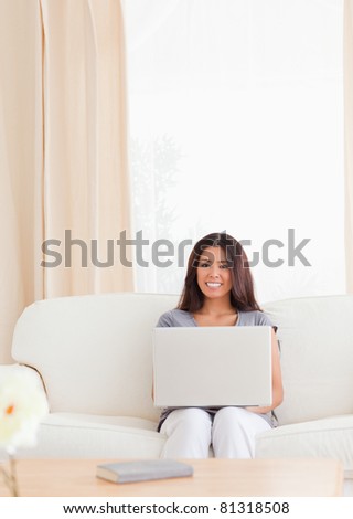 charming woman is sitting on a sofa with a notebook on her lap in the living room
