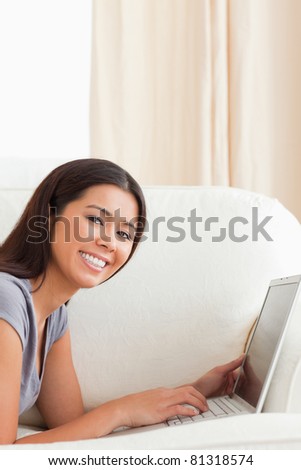 close up of a smiling woman lying on sofa with notebook looking into camera in living room