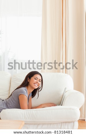 woman lying on sofa with notebook in front of her smiling into camera in living room