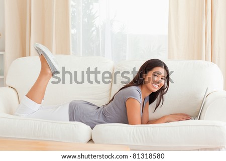 charming woman lying on sofa with notebook in front of her smiling into camera in living room