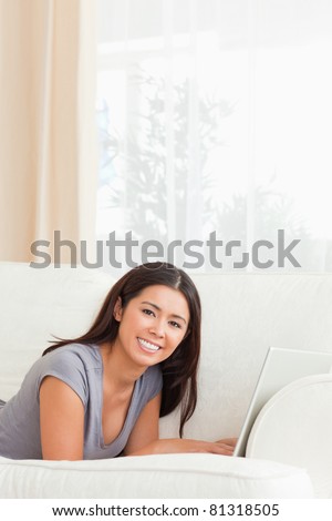 beautiful woman lying on sofa with notebook in front of her smiling into camera in living room