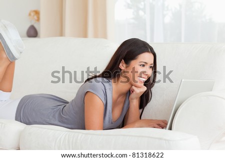 happy woman lying on sofa with notebook in front of her in living room