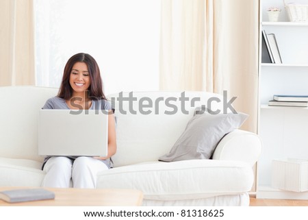 a woman is sitting on a sofa in the living room with her notebook on her lap