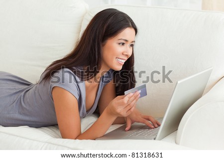 smiling woman with card in hand lying on sofa in living room