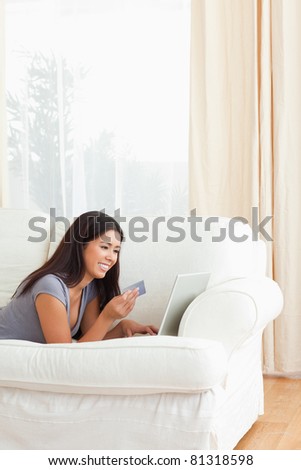 happy woman with card in hand lying on sofa in living room