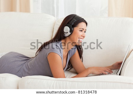 smiling woman with thumb up and earphones lying on sofa in living room