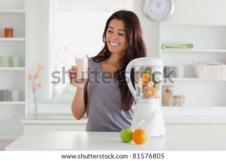 Attractive woman using a blender while holding a drink in the kitchen
