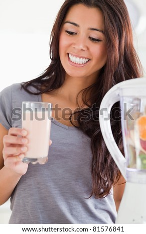 Pretty woman using a blender while holding a drink in the kitchen