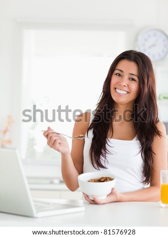 Gorgeous woman enjoying a bowl of cereal while relaxing with her laptop in the kitchen