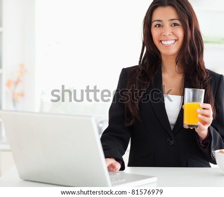 Beautiful woman in suit relaxing with her laptop while holding a glass of orange juice in the kitchen