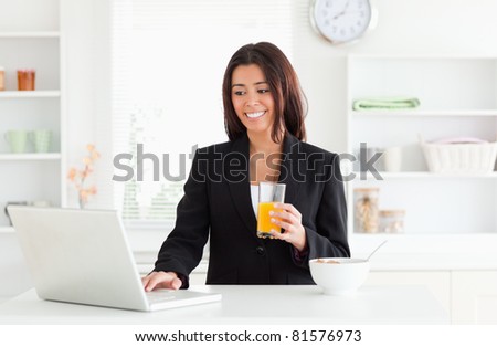 Charming woman in suit relaxing with her laptop while holding a glass of orange juice in the kitchen