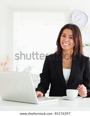 Good looking woman in suit enjoying a cup of coffee while relaxing with her laptop in the kitchen
