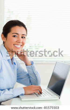 Charming woman working with her laptop and posing while sitting at the office