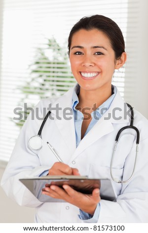 Attractive female doctor with a stethoscope writing on a notebook while standing in her office