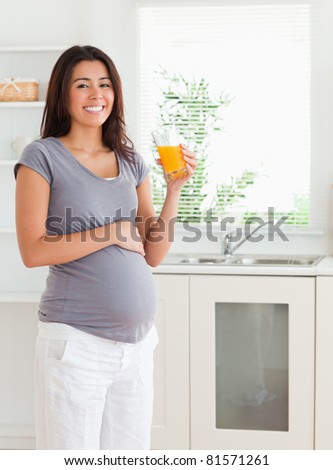 Gorgeous pregnant woman holding a glass of orange juice while standing in the kitchen