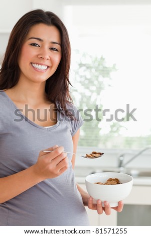 Gorgeous pregnant woman enjoying a bowl of cereal while standing in the kitchen