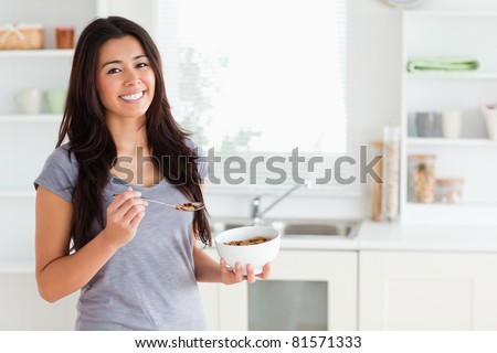 Lovely woman enjoying a bowl of cereal while standing in the kitchen