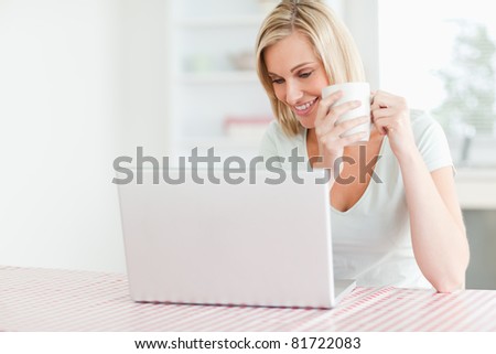 Close up of a woman holding coffee looking at the laptop in front of her in the kitchen