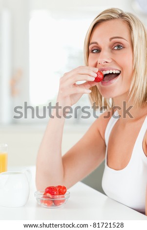 Young blonde woman sitting at table eats strawberries in the kitchen