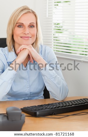 Charming blonde woman with chin on her hands behind a desk in an office