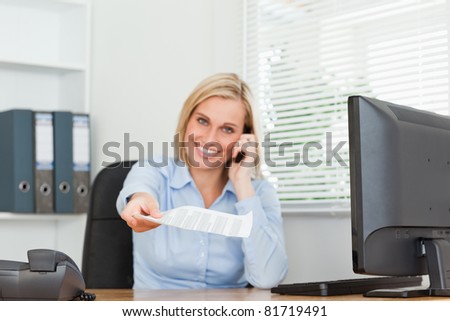 Businesswoman phoning and passing a paper looks into camera in her office