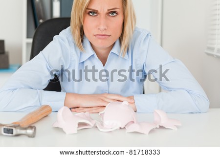 Sad woman sitting in front of an empty shattered piggy bank in her office
