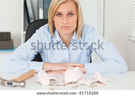 Sad woman sitting in her office in front of an shattered piggy bank with less in than expected