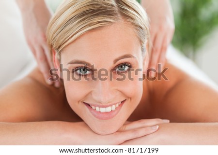 Close up of a smiling woman relaxing on a lounger during a massage looks into camera in a wellness center