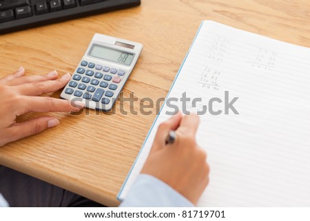 Feminine hands using a calculator and a pen in an office