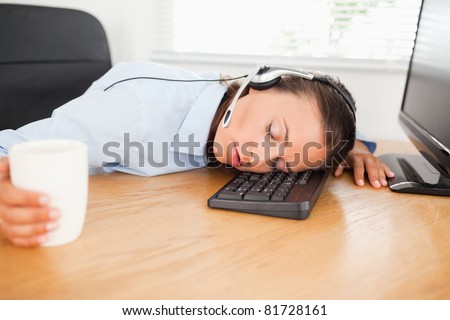 A businesswoman with a headset is sleeping in an office with her head on a keyboard