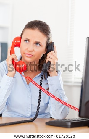 A businesswoman telephoning with two phones at the same time in an office