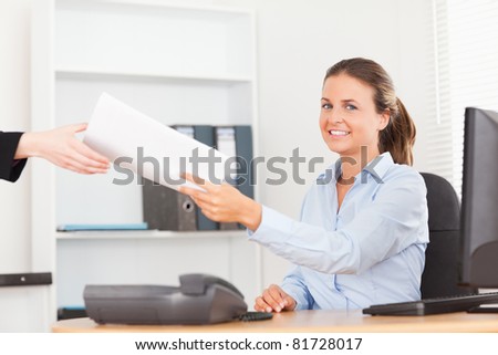 smiling businesswoman receiving a pile of paper looking into the camera in her office