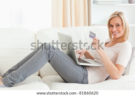 Cute woman buying on line while lying on a couch looking at the camera