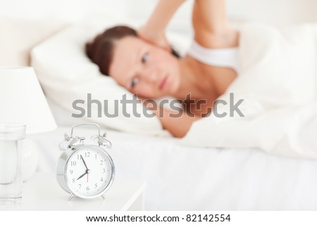 Good looking red-haired woman lying in bed not wanting to hear the alarm clock
