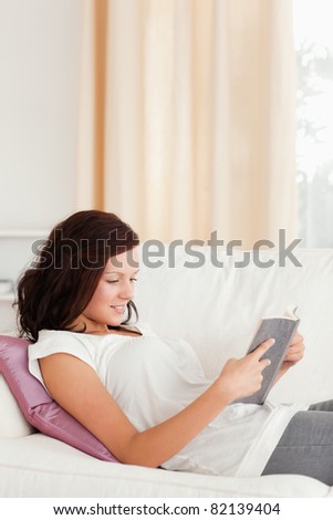 Young red-haired woman reading a book in her living room