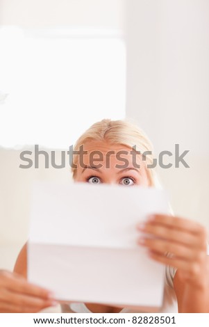 Shocked blond woman reading a letter in her living room