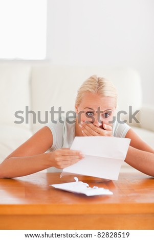 Shocked cute woman reading a letter in her living room