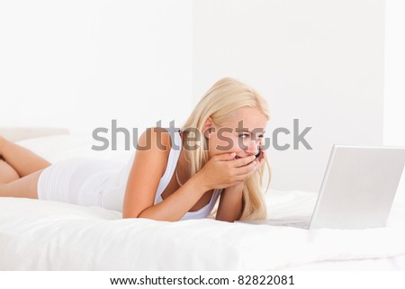 Woman laughing on the phone while using a laptop in her bedroom