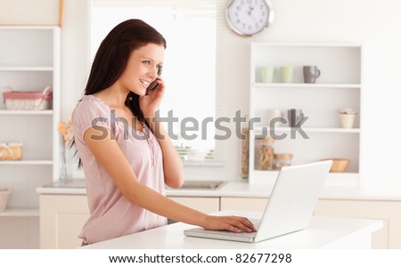 A telephoning woman is typing on her laptop