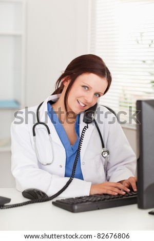 A smiling female doctor is telephoning and typing