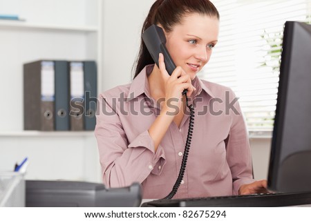 A businesswoman with telephone is looking to her screen