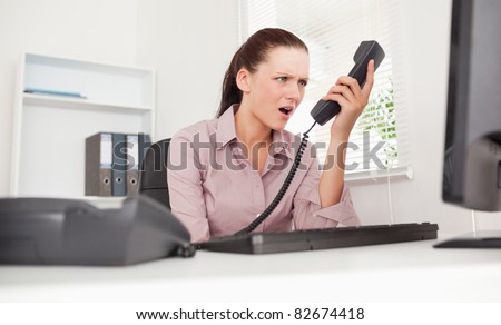A depressed businesswoman shouting at telephone in her office