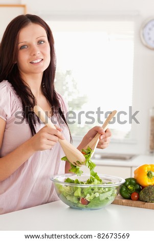 Smiling woman mixing a salad looking into the camera in a kitchen